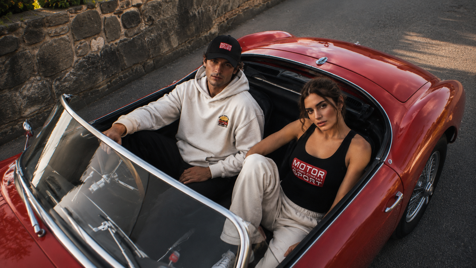 Male and female models in driver and passenger seat of red italian sports car wearing Palermo Company Motor Sport garments